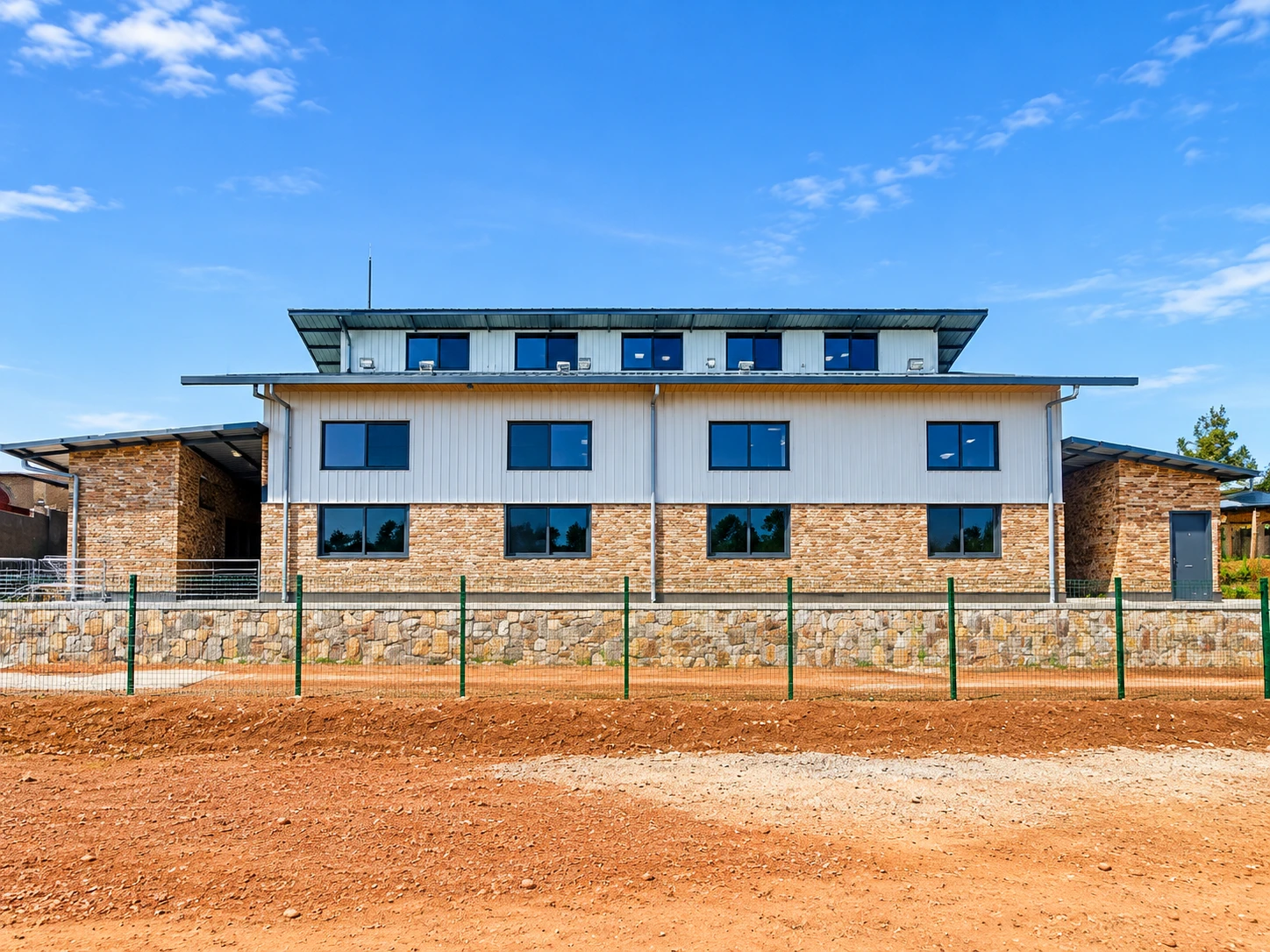 GS Bujyujyu school feeding kitchen for Solid Africa in Rwamagana District, a two-storey building with stone-clad base, metal cladding and stone retaining wall, built by Sezibera Construction